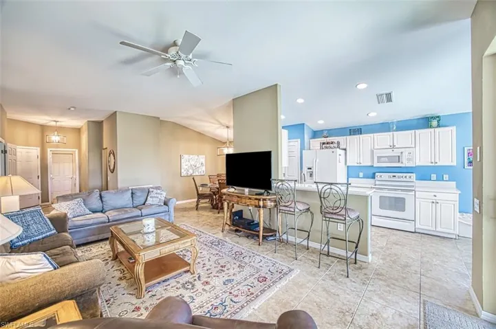 Living area with light tile patterned floors, a ceiling fan, lofted ceiling, and recessed lighting