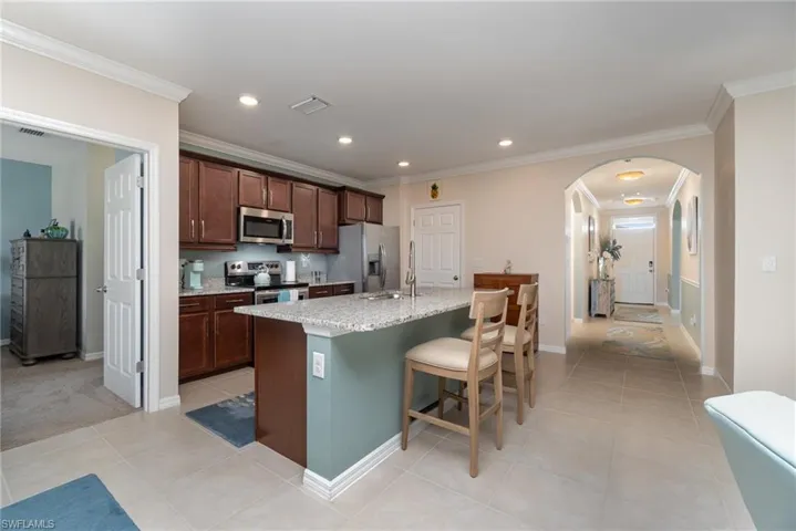 Kitchen with a center island with sink, crown molding, stainless steel appliances, light stone countertops, and a kitchen breakfast bar