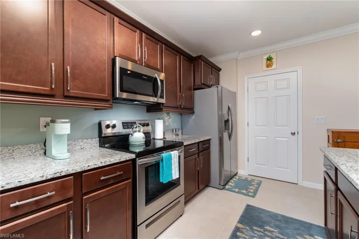 Kitchen with stainless steel appliances, light tile flooring, crown molding, and light stone counters