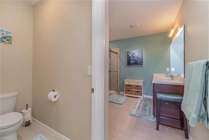 Bathroom with toilet, vanity, an enclosed shower, and tile flooring