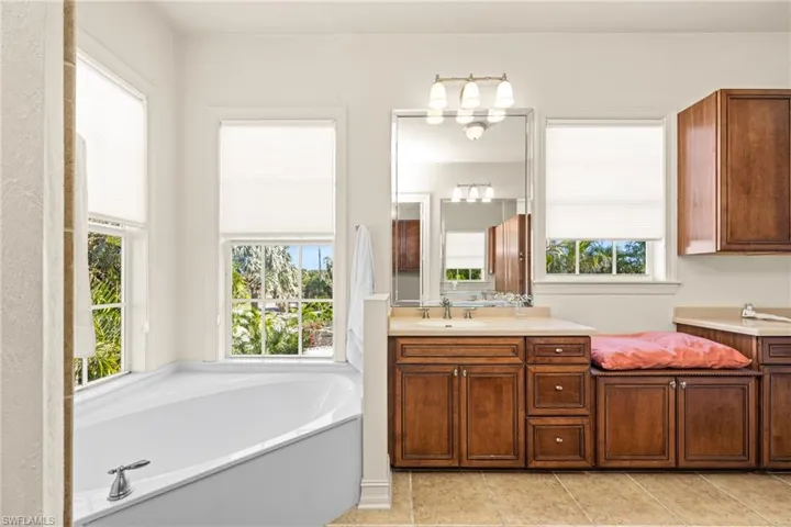 Bathroom with dual vanities, tile patterned floors, and a bathing tub