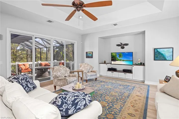 Living room with a raised ceiling, ceiling fan, plenty of natural light, and light hardwood / wood-style flooring