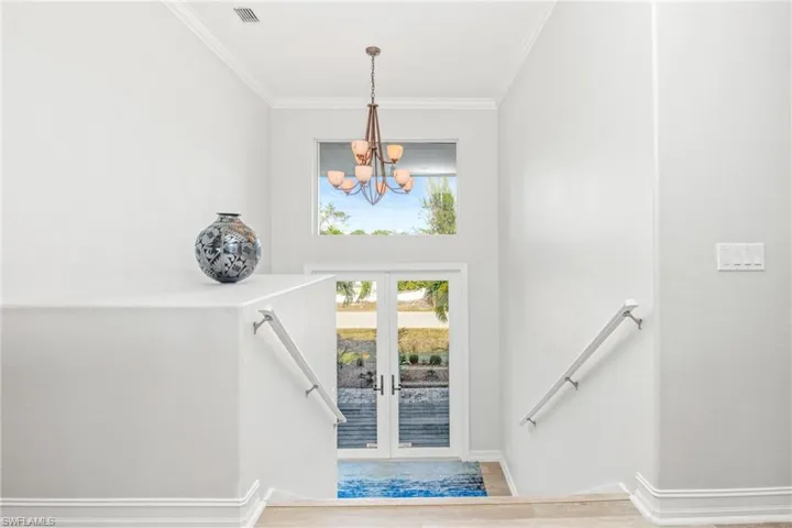 Stairway featuring hardwood / wood-style floors, an inviting chandelier, french doors, and crown molding