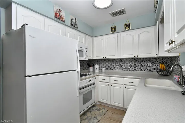 Kitchen with white cabinets, decorative backsplash, white appliances, and light tile flooring.