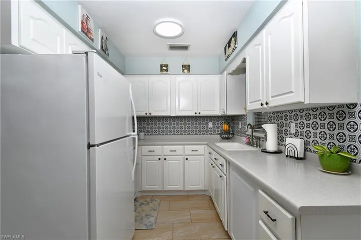 Kitchen with white cabinets, decorative backsplash, white appliances, and light tile flooring