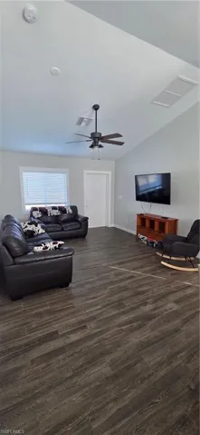 Living area with dark wood-type flooring, a ceiling fan, and vaulted ceiling