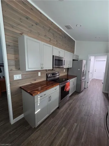 Kitchen with wooden counters, stainless steel appliances, white cabinetry, dark wood finished floors, and wood walls