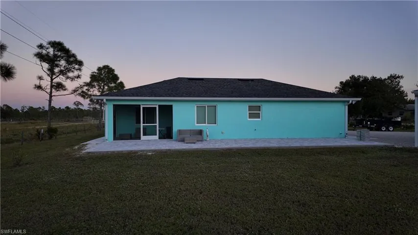 Back of property at dusk featuring a yard, a patio, stucco siding, and a shingled roof