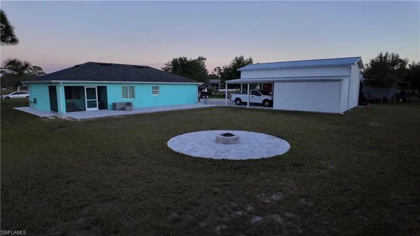 Back of property at dusk featuring a lawn, an outdoor fire pit, a patio, and a metal roof and a fire pit