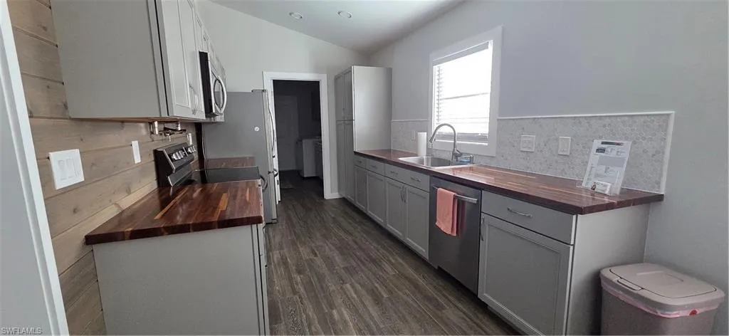 Kitchen featuring wood counters, gray cabinets, dishwasher, dark wood finished floors, and tasteful backsplash