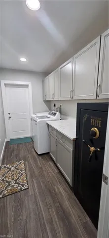 Washroom with dark wood finished floors, washer and dryer, recessed lighting, and cabinet space
