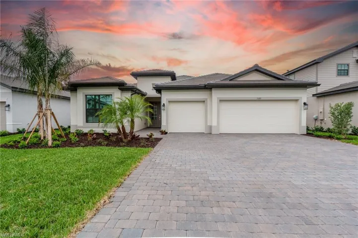 Modern stucco exterior featuring a two-car garage, paver driveway, manicured lawn, and established palm trees