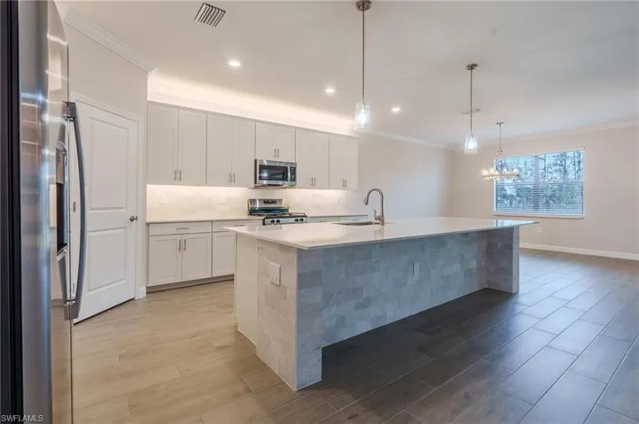 Open-concept living space featuring wood-finish tile flooring, a contemporary kitchen island with a stone facade, and a tray ceiling with a modern ceiling fan