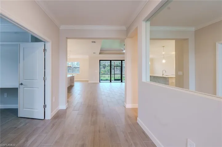 Spacious kitchen featuring an elongated island with pendant lighting, white shaker cabinetry, stainless steel appliances, light countertops, and wood-finish flooring