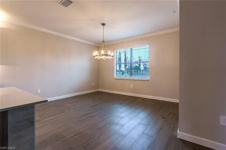 Spacious room featuring wood-finish flooring, a tray ceiling with crown molding, a ceiling fan with integrated lighting, and a large window with blinds