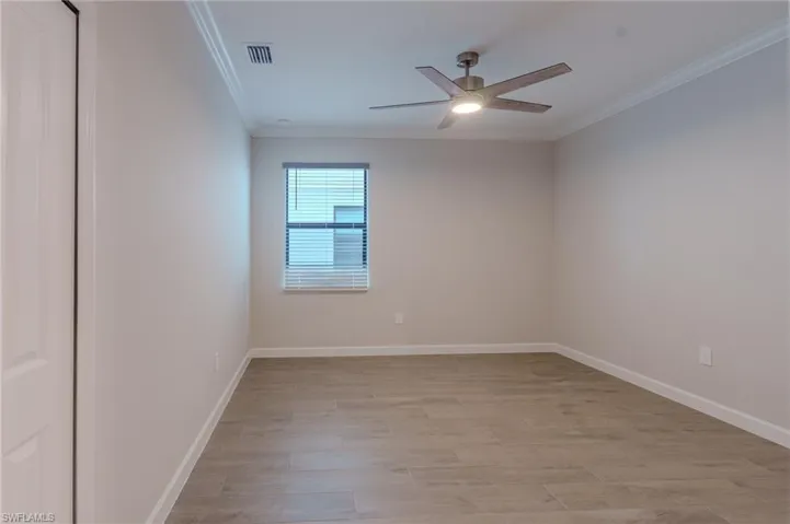 Spacious room featuring wood-finish flooring, a window with horizontal blinds, crown molding, and a modern ceiling fan with integrated lighting