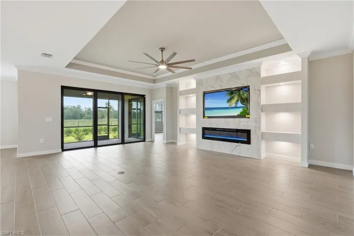 Spacious living area featuring light wood-finish flooring and a tray ceiling with a built-in ceiling fan