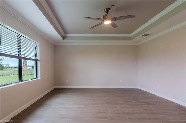 Spacious room featuring wood-finish tile flooring, a tray ceiling with crown molding, and a modern ceiling fan with integrated lighting