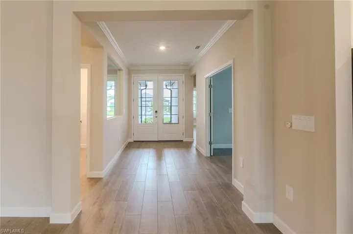 Spacious room featuring wood-finish flooring, a contemporary ceiling fan with integrated lighting, crown molding, and a large window with horizontal blinds
