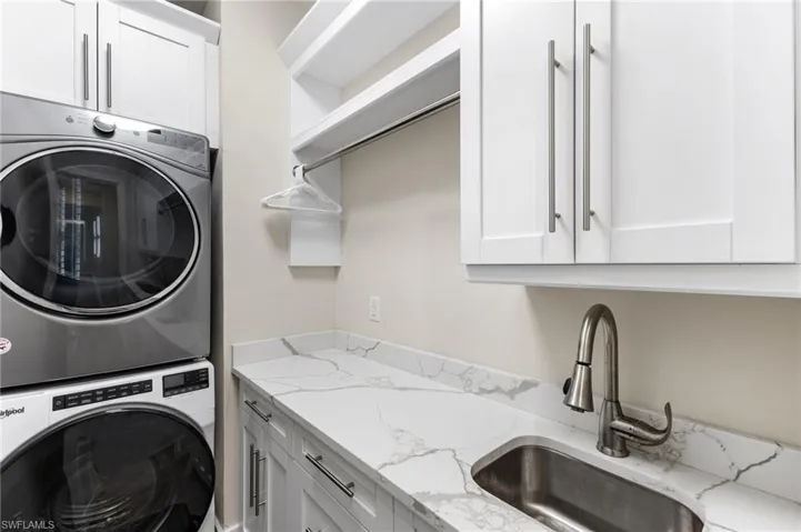 Clothes washing area with sink, stacked washing maching and dryer, and cabinets