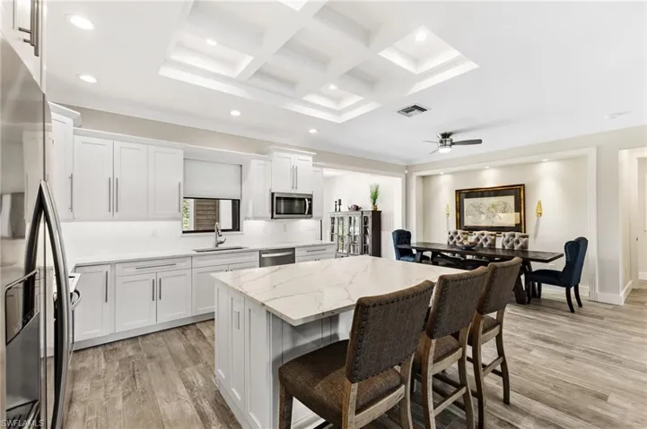 Kitchen with stainless steel appliances, light hardwood / wood-style flooring, white cabinetry, and coffered ceiling