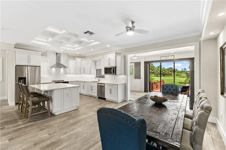 Kitchen with a center island, light wood-type flooring, appliances with stainless steel finishes, wall chimney exhaust hood, and coffered ceiling