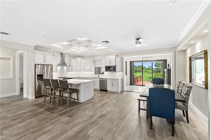 Kitchen featuring appliances with stainless steel finishes, light hardwood / wood-style floors, coffered ceiling, a kitchen island, and wall chimney range hood
