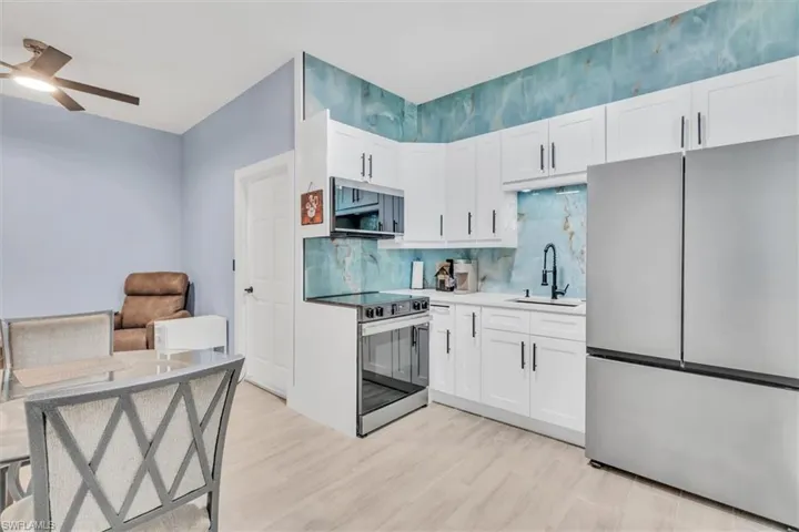 Kitchen with stainless steel appliances, a sink, a ceiling fan, white cabinetry, and tasteful backsplash