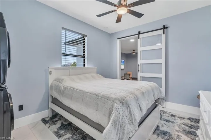 Bedroom featuring a barn door, baseboards, ceiling fan, and marble look tiles