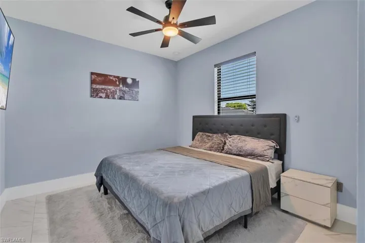 Bedroom featuring marble look tile flooring, ceiling fan, and baseboards
