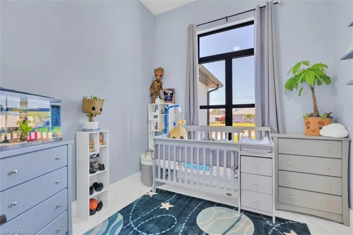 Bedroom featuring marble look tile flooring, a nursery area, and baseboards