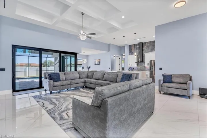 Living area with a towering ceiling, coffered ceiling, baseboards, light marble finish floors, and a ceiling fan