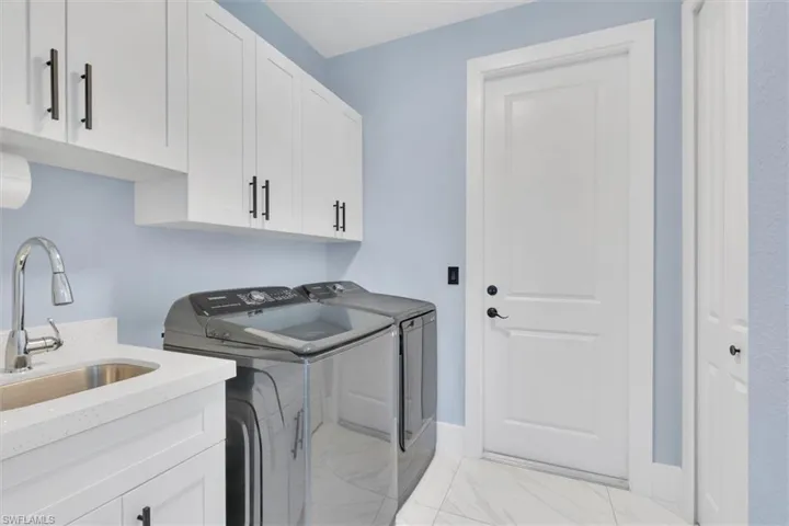 Clothes washing area with independent washer and dryer, light marble finish floors, cabinet space, and baseboards