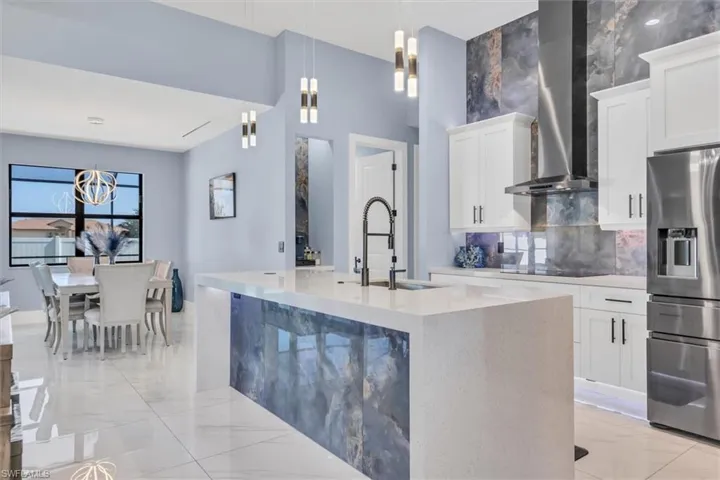 Kitchen with stainless steel fridge, a sink, wall chimney range hood, and light marble finish floors