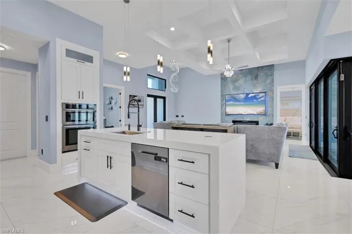 Kitchen with dishwasher, double oven, a sink, light marble finish flooring, and coffered ceiling
