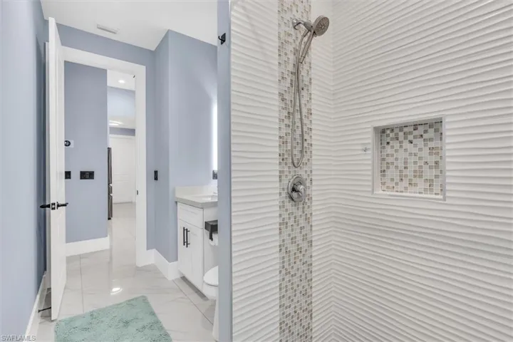 Bathroom featuring a tile shower, vanity, marble look tile flooring, and baseboards