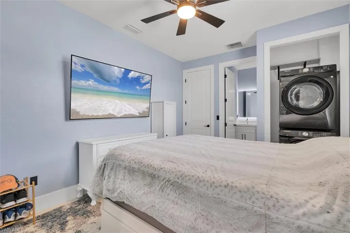 Bedroom with stacked washer and clothes dryer, baseboards, a sink, ensuite bath, and a ceiling fan