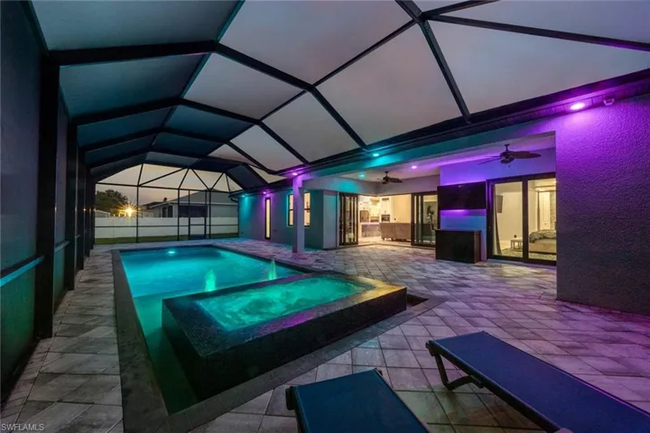 View of swimming pool featuring ceiling fan, a patio area, an in-ground hot tub, and glass enclosure