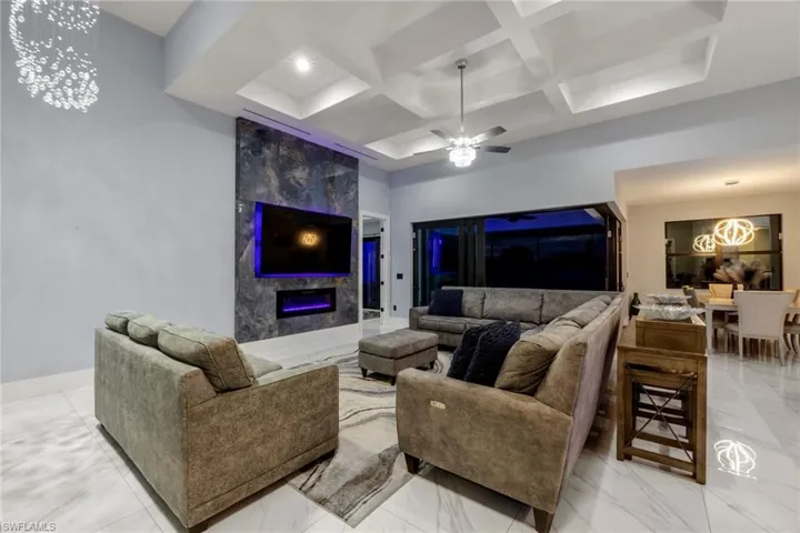 Living room with coffered ceiling, light marble finish floors, a fireplace, beam ceiling, and a chandelier