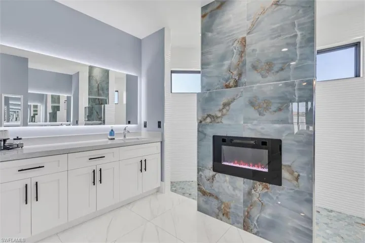 Full bath with a tiled fireplace, walk in shower, marble finish flooring, and vanity