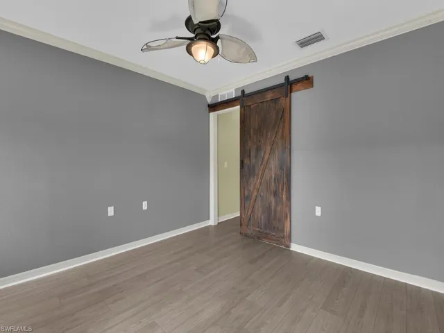 Unfurnished bedroom featuring a barn door, crown molding, a ceiling fan, and wood finished floors