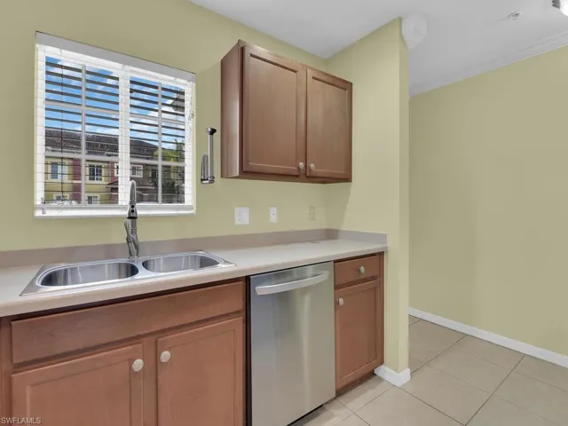 Kitchen with dishwasher, light countertops, light tile patterned floors, wood finish cabinets, and crown molding