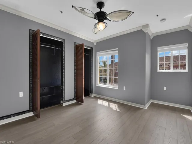 Unfurnished bedroom with ornamental molding, two closets, wood finished floors, and ceiling fan