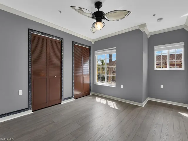 Unfurnished bedroom featuring ornamental molding, two closets, light wood-style flooring, and ceiling fan