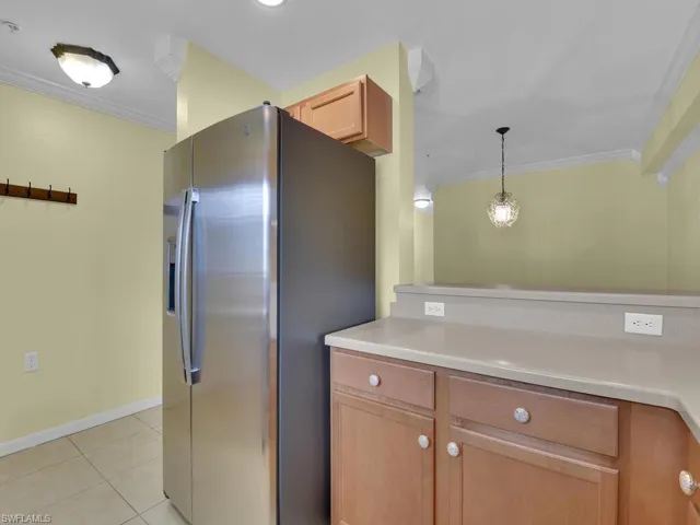 Kitchen with crown molding, stainless steel fridge with ice dispenser, light countertops, light wood finish cabinets, and pendant lighting