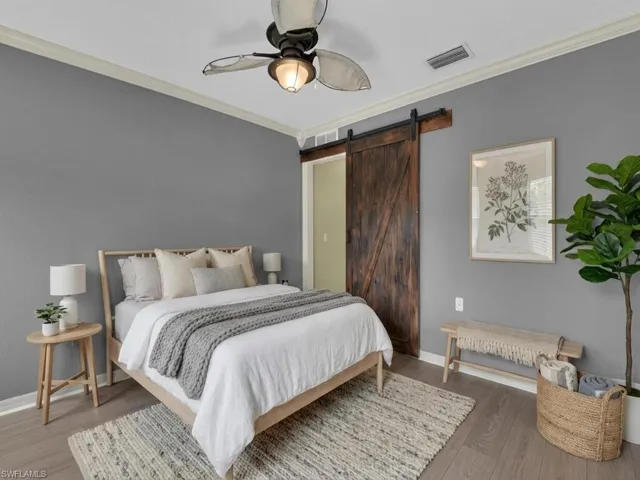 Bedroom with a barn door, ornamental molding, wood finished floors, and ceiling fan