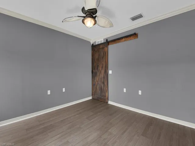 Spare room featuring crown molding, a barn door, a ceiling fan, and wood finished floors