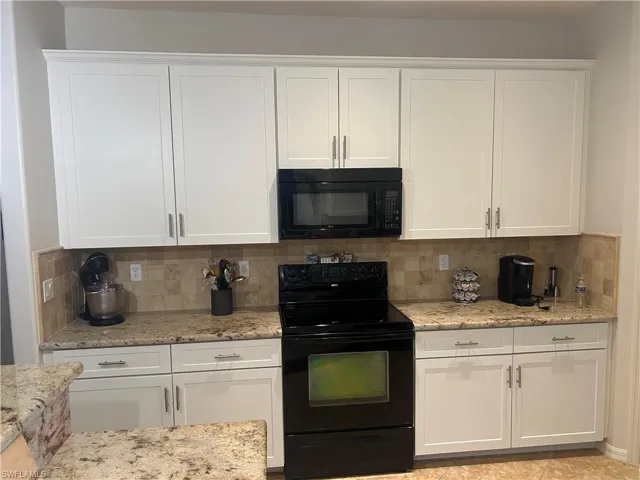 Kitchen featuring light stone counters, white cabinetry, and backsplash