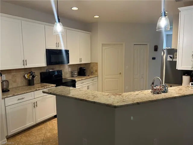 Kitchen with black appliances, decorative backsplash, a breakfat bar, white cabinetry, and recessed lighting