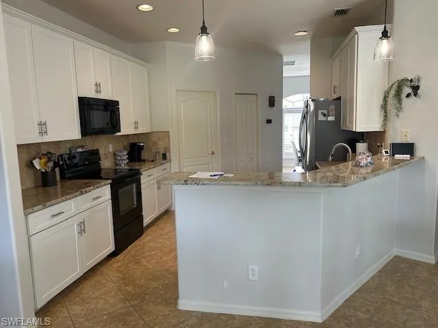 Kitchen featuring stainless steel refrigerator, black appliances, white cabinets, and light granite countertops